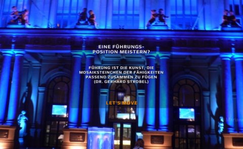 Eine Führungsposition meistern? - Das Bild zeigt die blau-orange beleuchtete Börse während der Luminale in Frankfurt und das Zitat "Führung ist die Kunst, die Mosaiksteinchen der Fähigkeiten passend zusammen zu fügen" (Dr. Gerhard Strobel)